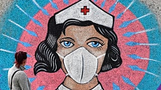 A woman looks at a coronavirus graffiti by street artist 'Uzey' showing a nurse with a face mask on a wall during a walk in Hamm, Germany, on Easter Monday, April 13, 2020.