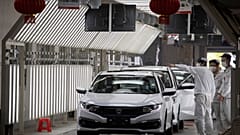 In this April 8, 2020, photo, workers wearing masks against the coronavirus chat near finished cars rolled out at the Dongfeng Honda Automobile Co., Ltd factory in Wuhan.