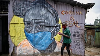 A boy wearing a face mask as he walks past an informational mural warning people about the risk of the new coronavirus, painted by artists from the Mathare Roots youth group