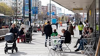 Des gens mangent des glaces dans un café en plein air alors que d'autres passent dans le centre de Stockholm, en Suède, le lundi 20 avril 2020.