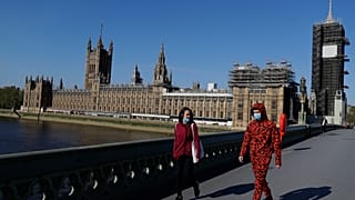 People wear masks as they walk near Britain's Houses of Parliament as it goes back to work, London, Tuesday, April 21, 2020.