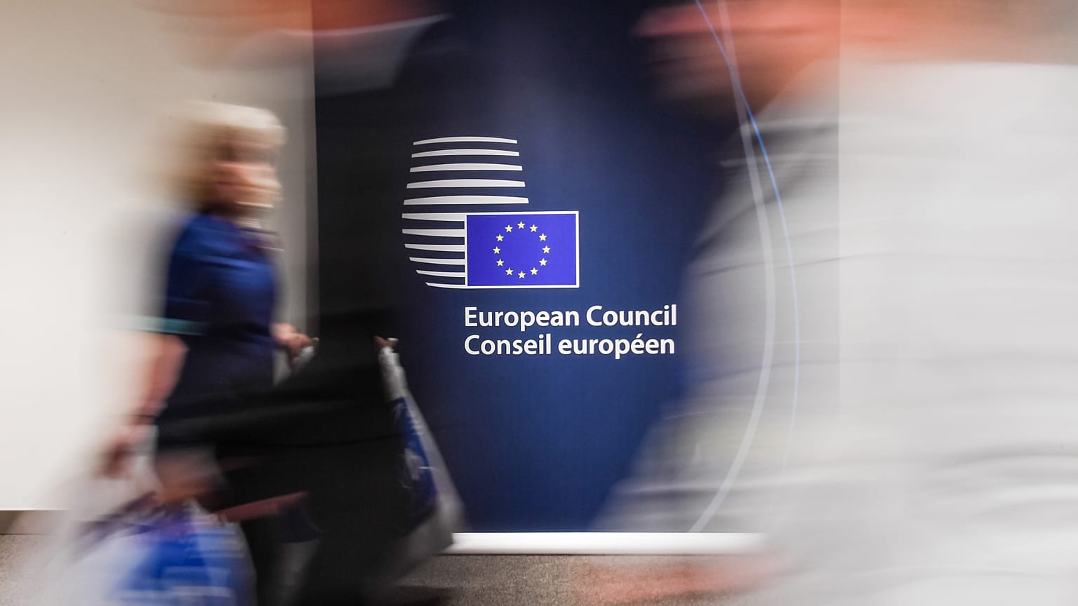 People walk by a sign in English and French in the press room at an EU summit in Brussels on Tuesday, June 28, 2016. 