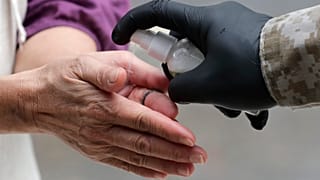 A woman is given hand sanitizer as she waits outside of Marcus Samuelsson's Red Rooster Restaurant for a free meal during the new coronavirus pandemic