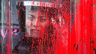 A police officer stands behind her riot shield covered in red paint during an International Women's Day march in Mexico City's main square, Sunday, March 8, 2020.