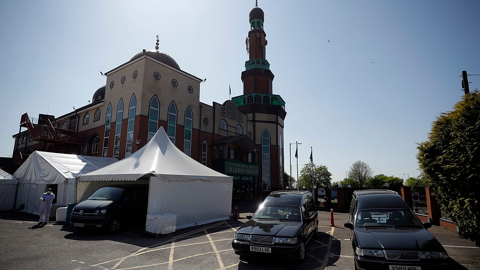 A volunteer wearing protective clothing and a face mask to protect from coronavirus, walks through the car park of Central Jamia Mosque Ghamkol Sharif in Birmingham, England