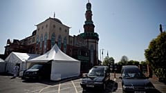 A volunteer wearing protective clothing and a face mask to protect from coronavirus, walks through the car park of Central Jamia Mosque Ghamkol Sharif in Birmingham, England