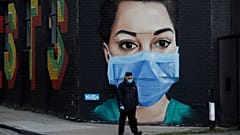 A man wearing a face mask and gloves to protect from coronavirus walks past a recently painted mural by professional street artist David Speed and the Graffiti Life collective