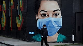 A man wearing a face mask and gloves to protect from coronavirus walks past a recently painted mural by professional street artist David Speed and the Graffiti Life collective