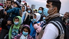 Refugees and migrants wearing masks to prevent the spread of the coronavirus, wait to get on a bus after their arrival at the port of Piraeus, near Athens
