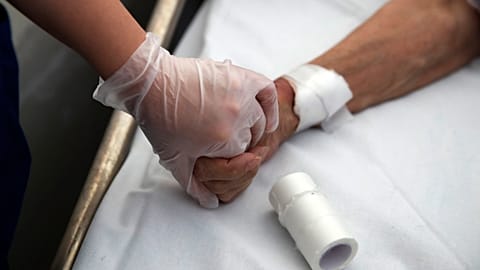 A medical worker holds the hand of a patient in Greece in 2020.