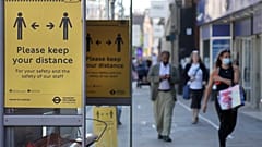 Signs advise people to social distance on a bus stop along a high street, in London
