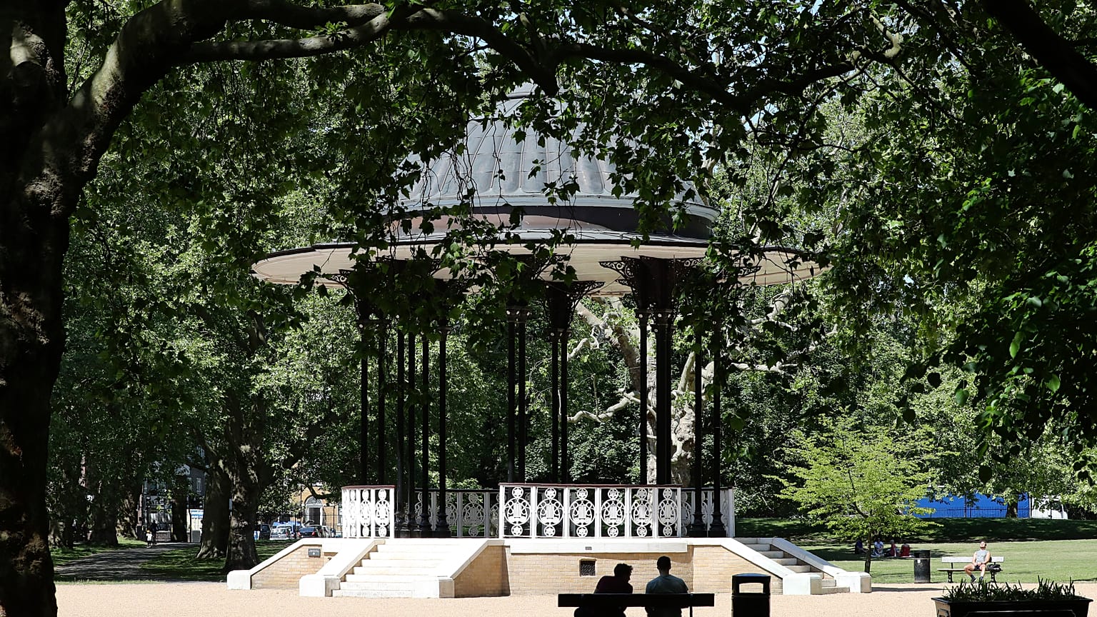 People sit on benches near the bandstand in Southwark Park in London, Tuesday, May 19, 2020