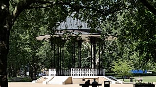 People sit on benches near the bandstand in Southwark Park in London, Tuesday, May 19, 2020