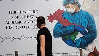 A man looks at a giant image of a drawing by Venetian artist Franco Rivolli showing a doctor with wings on her back cradling Italy