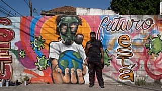 Graffiti artist Angelo Campos poses for a photo by his mural referencing the COVID-19 pandemic which he said he painted in honor of health workers in Rio de Janeiro, Brazil