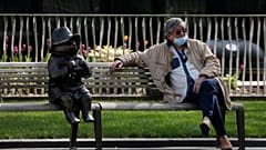 A man relaxes on a bench in London, next to a sculpture of Paddington Bear, as the country is in lockdown to help curb the spread of the coronavirus, Wednesday, April 15, 2020
