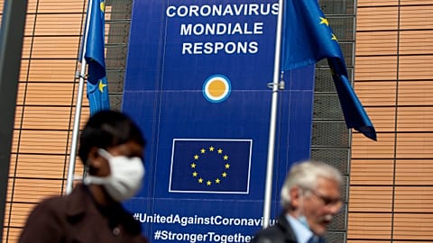 A woman wearing mouth mask, to prevent against the spread of the coronavirus, COVID-19, walks past EU headquarters in Brussels, Thursday, May 7, 2020. 