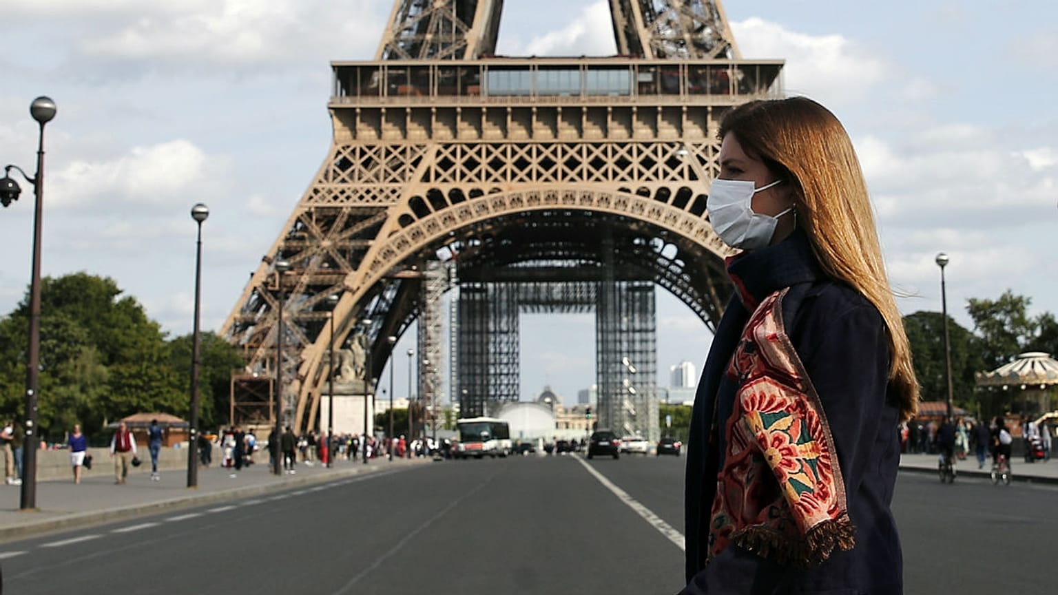 A woman wearing protective face mask walks next to the Eiffel Tower in Paris