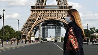 A woman wearing protective face mask walks next to the Eiffel Tower in Paris