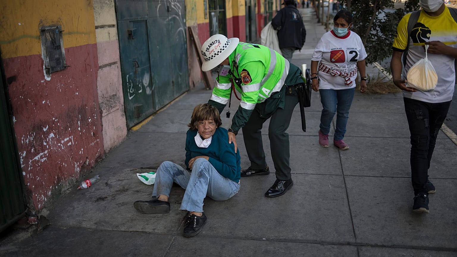 Un policía ayuda a una mujer tendida en una calle de Lima, Perú