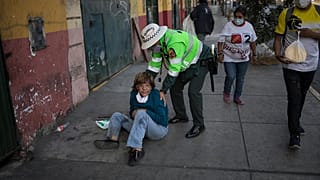 Un policía ayuda a una mujer tendida en una calle de Lima, Perú