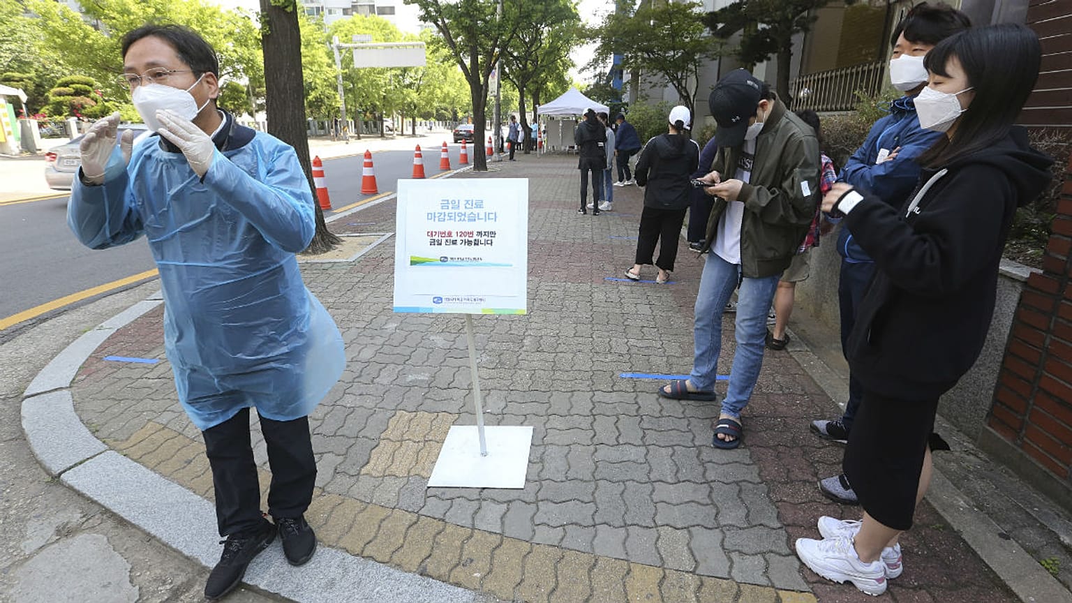 A medical staff, left, wearing a face mask shouts that the COVID-19 testing is over as people waiting for the test at a hospital in Seoul