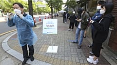 A medical staff, left, wearing a face mask shouts that the COVID-19 testing is over as people waiting for the test at a hospital in Seoul