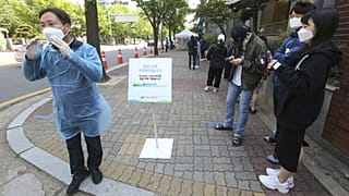 A medical staff, left, wearing a face mask shouts that the COVID-19 testing is over as people waiting for the test at a hospital in Seoul