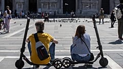 A woman and a man relax sitting on their scooters at the Duomo square, in Milan, Italy, Monday, May 25, 2020.