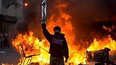 A protester holds a skateboard in front of a fire in Los Angeles