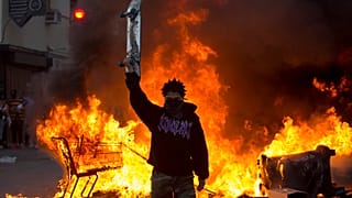 A protester holds a skateboard in front of a fire in Los Angeles