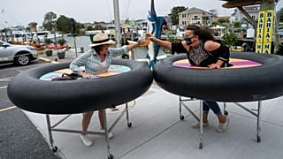 Restaurant guests use social distancing devices made of rubber tubing as Fish Tails Bar and Grill opens for in person dining during the pandemic. Ocean City, Maryland, USA