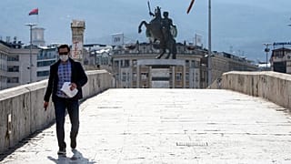 A man wearing a face mask and protective gloves walks across a usually crowded bridge in downtown Skopje