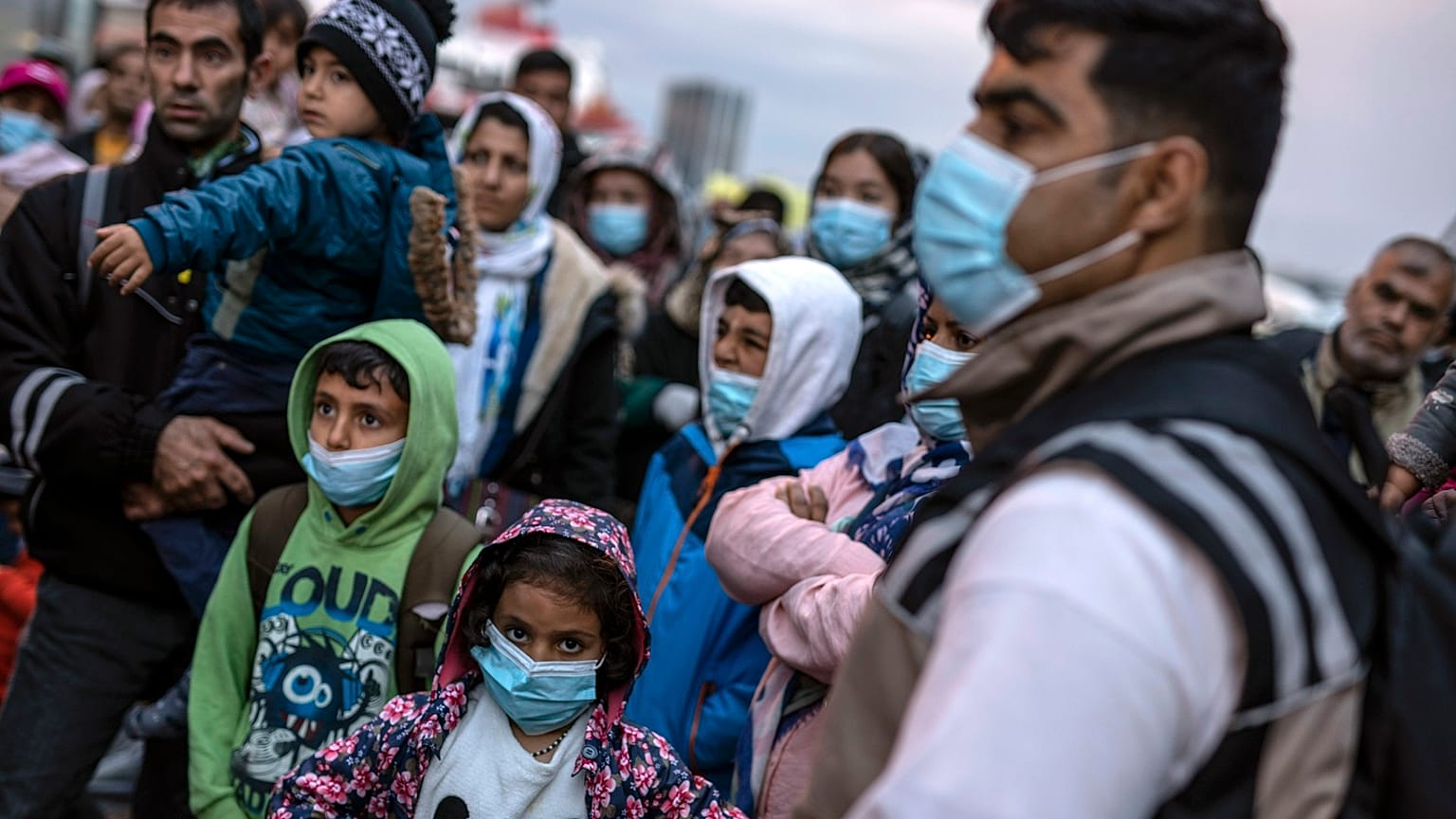 Refugees and migrants wearing masks to prevent the spread of the coronavirus, wait to get on a bus after their arrival at the Greek port of Piraeus