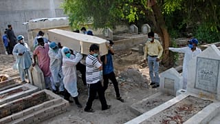 Rescue workers and family members carry the casket of Khursheed Bibi, who died due to coronavirus, for her burial at a cemetery in Hyderabad, Pakistan