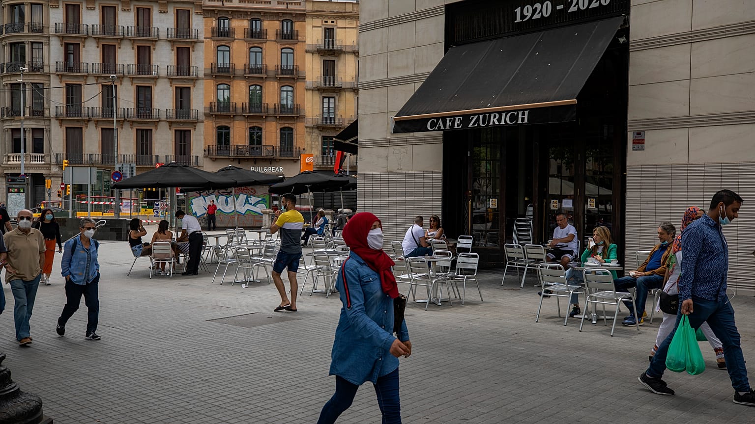 In this Monday, June 1, 2020 photo, people walk past a terrace bar with local customers in Barcelona downtown.