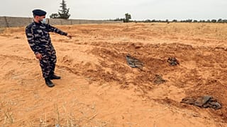 A member of security forces affiliated with the Libyan Government of National Accord (GNA)'s Interior Ministry points at the reported site of a mass grave in town Tarhuna