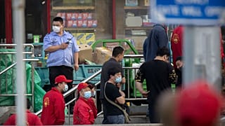 Police and security officials watch as workers line up outside a building holding a beef and lamb market in Beijing that was closed by authorities Friday, June 12, 2020