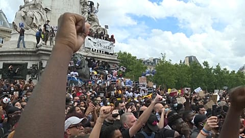 Mid shot anti-racism protesters in Place de la République raise their fists