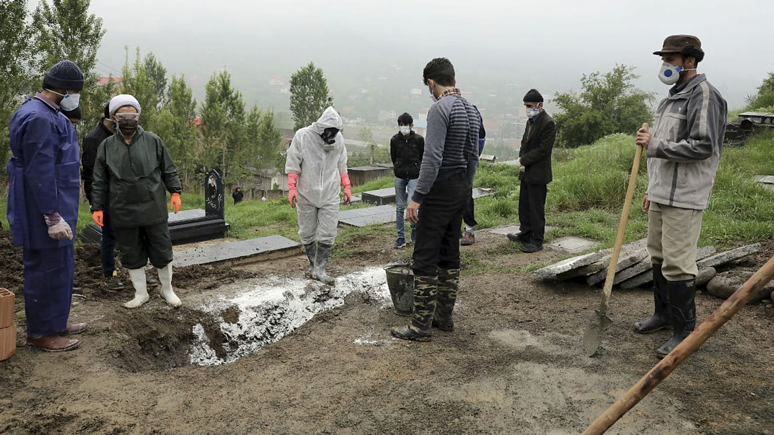 People wearing protective clothing, masks and gloves, pray during the funeral of a victim who died from the new coronavirus
