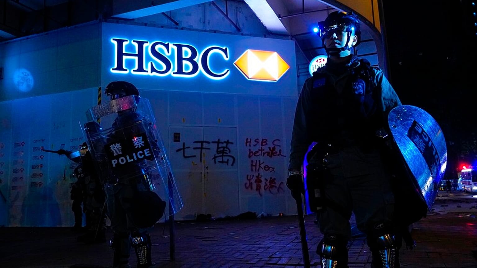 Police stand guard in front of a vandalized HSBC bank