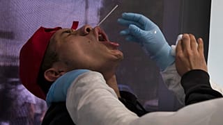 عامل من القطاع الصحي يحاول أخذ عينة للاختبار من عامل في أحد أسواق مدينة مكسيكو 