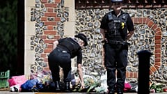 A Police officer places flowers from a woman at the scene of a fatal multiple stabbing attack in Forbury Gardens, central Reading, England, Monday June 22, 2020.