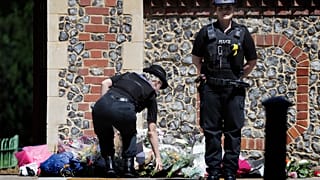 A Police officer places flowers from a woman at the scene of a fatal multiple stabbing attack in Forbury Gardens, central Reading, England, Monday June 22, 2020.