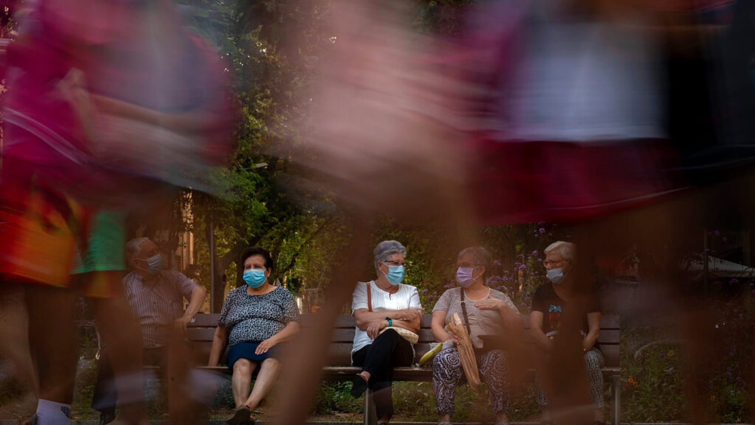 Pedestrians walk past people sit in a bench in Barcelona, Spain, Sunday, June 21