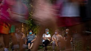 Pedestrians walk past people sit in a bench in Barcelona, Spain, Sunday, June 21