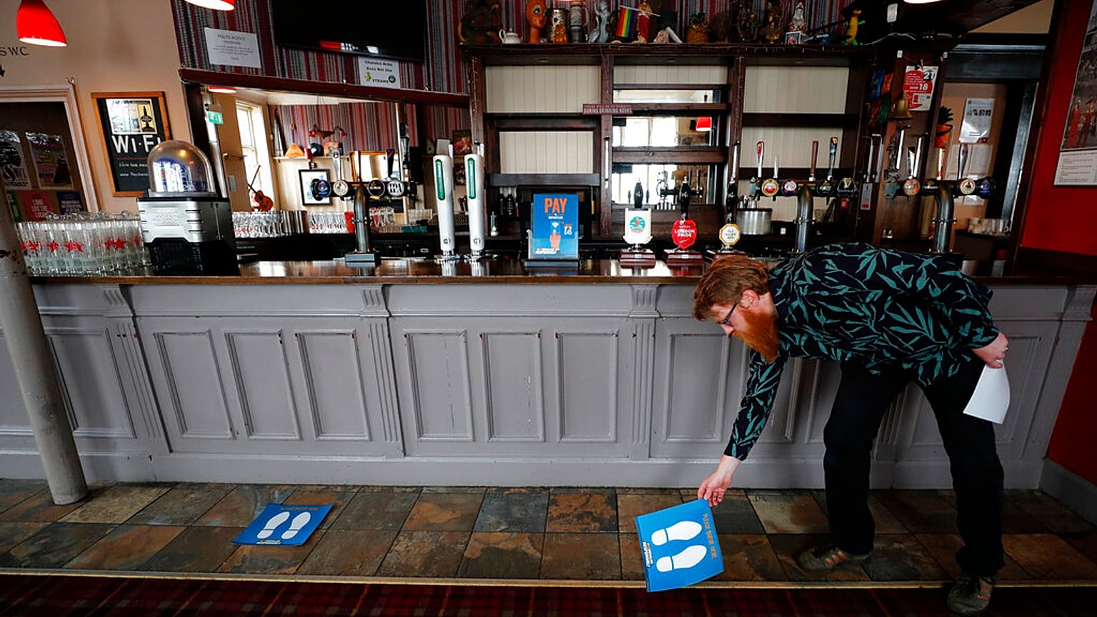 Owner Are Kjetil Kolltveit from Norway places markers for social distancing on the front of the bar at the Chandos Arms pub in London, Wednesday, July 1, 2020.