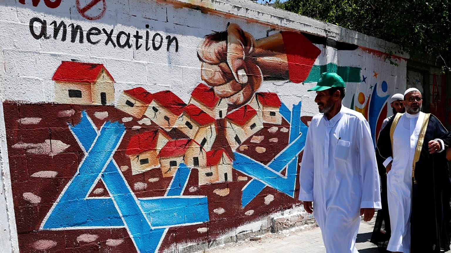 Hamas supporters pass a mural against Israel's plan to annex parts of the West Bank and U.S. President Donald Trump's mideast initiative