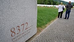 Visitors pray at the memorial cemetery in Potocari, near Srebrenica, Bosnia, Tuesday, July 7, 2020. Writing on stone translates "8372 victims, number is not final'. 