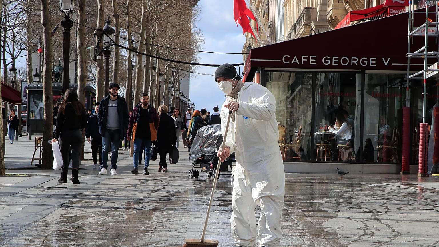 A masked worker wipes the pavement of the Champs Elysees avenue in Paris, Friday, March 13, 2020.
